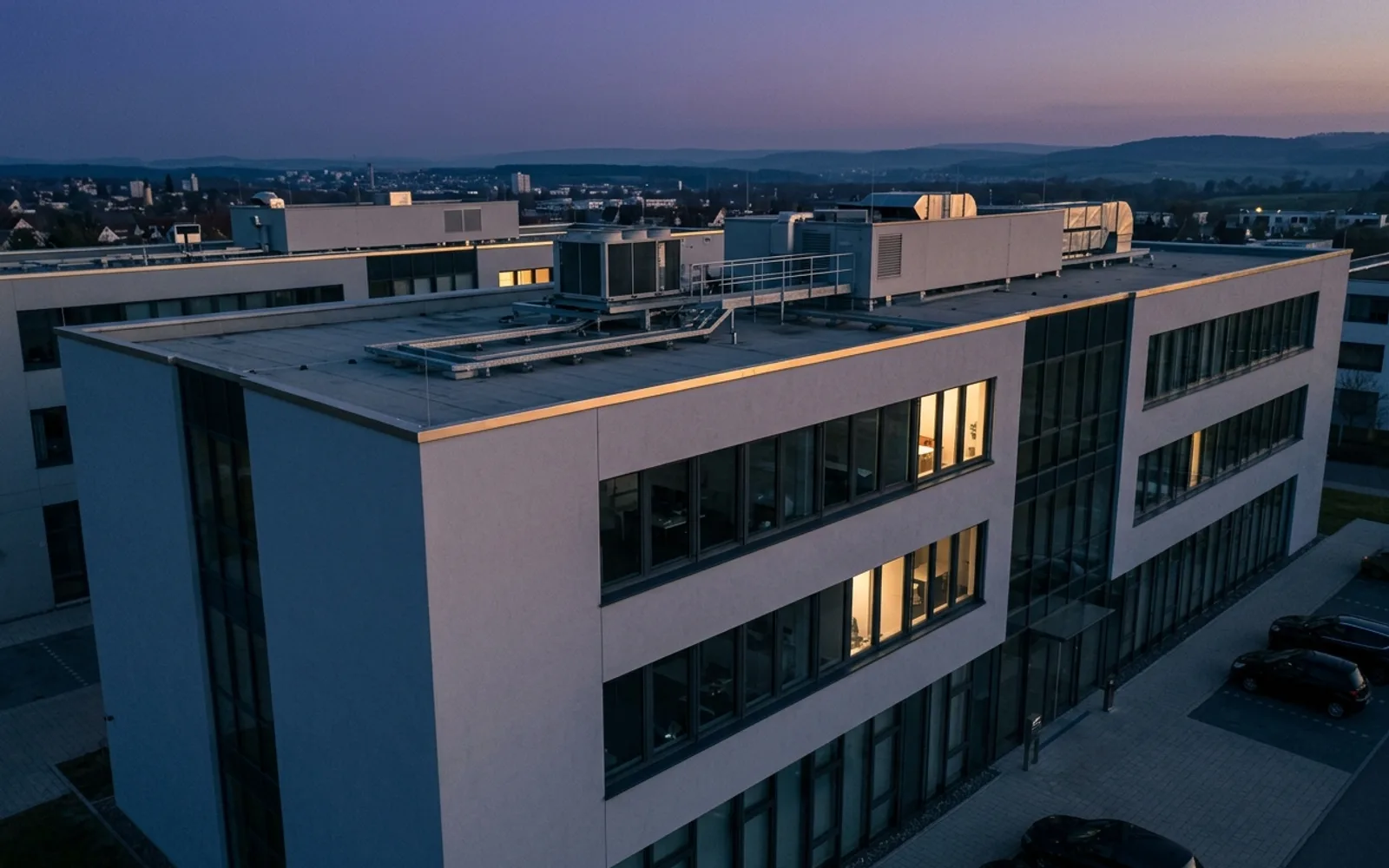 Bürogebäude mit Putz- und Glasfassade und Dachaufbauten, Drohnenaufnahme in der Dämmerung